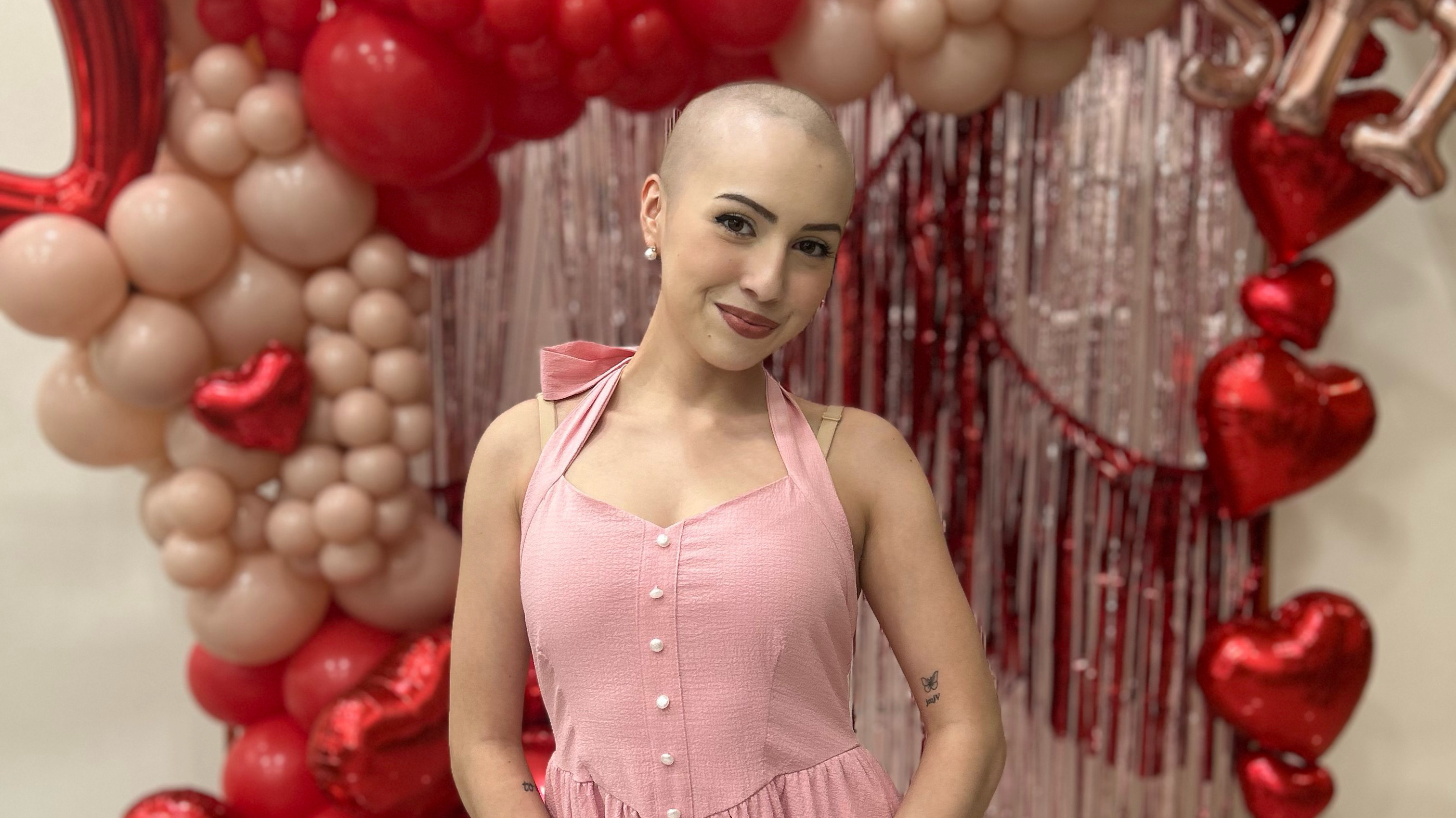 Valerie with a shaved head standing in front of balloons