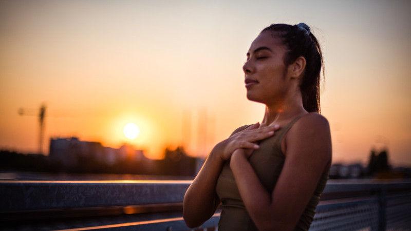Stock image of woman with hands on chest, breathing, in front of sunset
