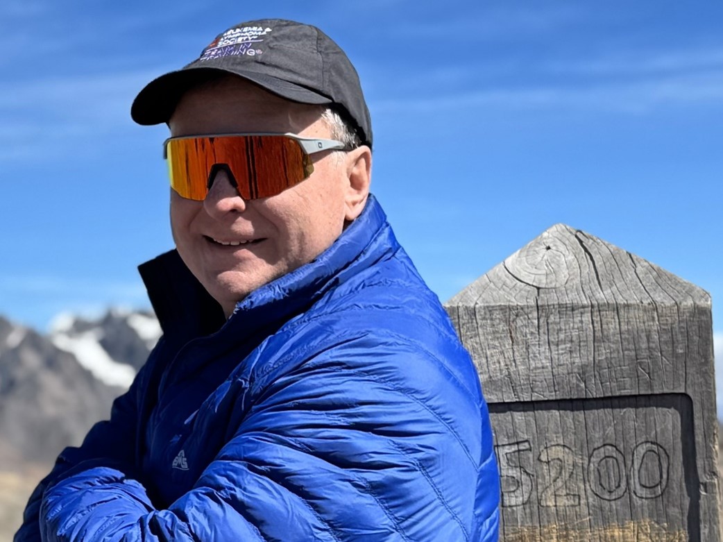 A man with sunglasses stands at a mountain peak at 5,200 meters altitude