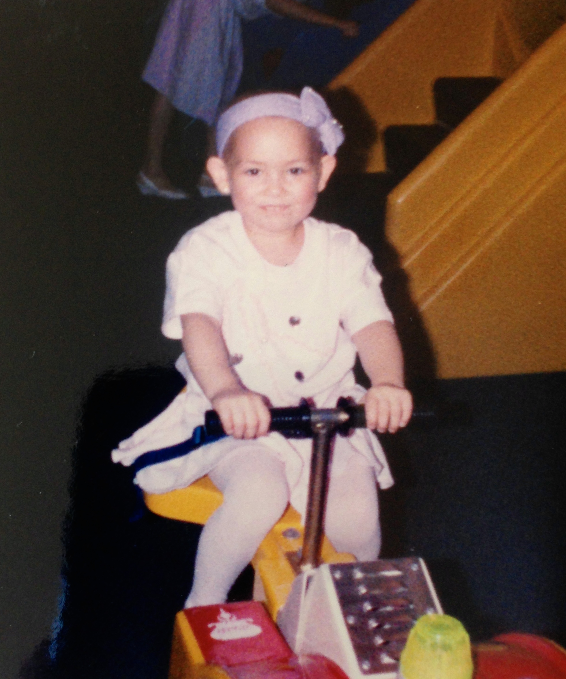 Little girl with leukemia on a scooter with a purple ribbon headband