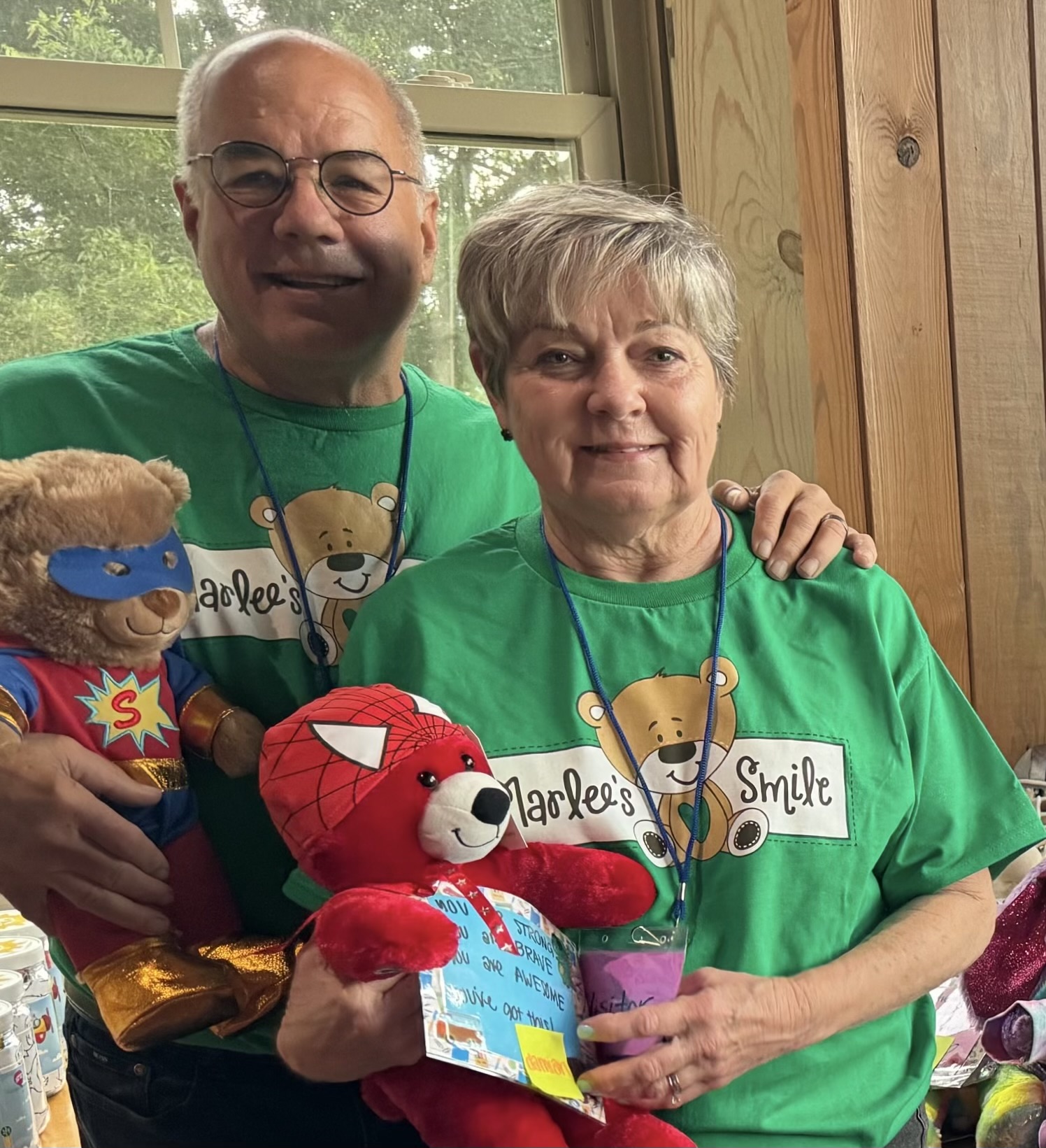 Older man with leukemia with his wife in green bear t-shirts holding stuffed bears