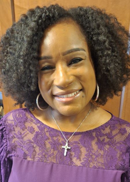 middle aged black woman wearing hoop earrings and a purple lace dress.