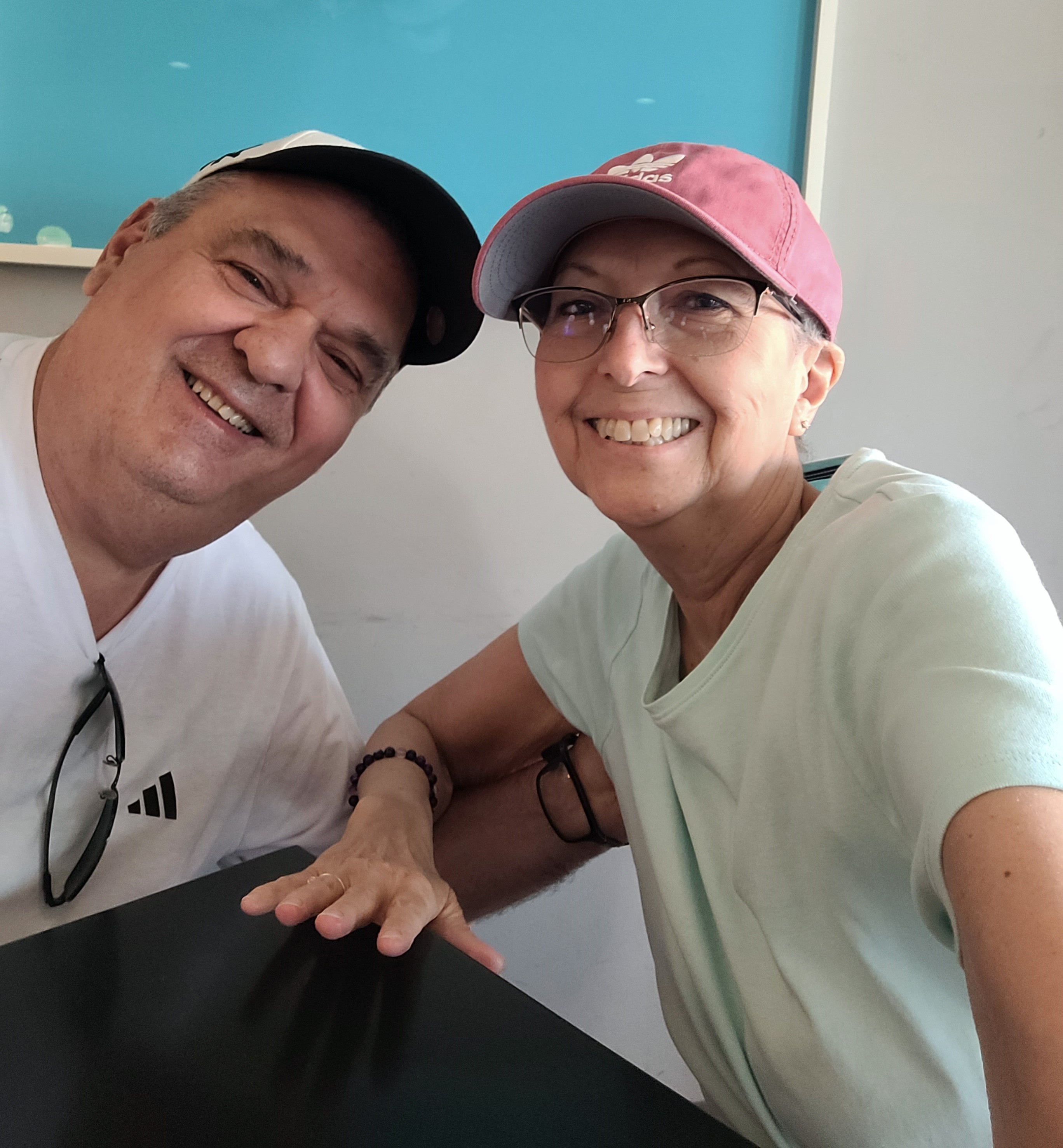 older white couple he has on a ball cap and white t-shirt and she has on pink ball cap and glasses and a white t-shirt