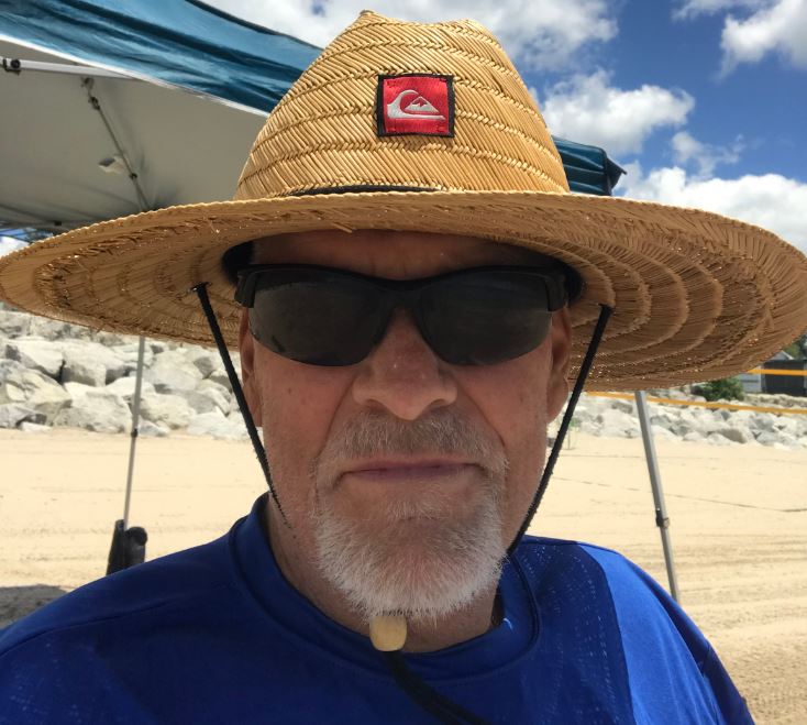 older white man with beard and mustache wearing sunglasses a strawhat and blue t-shirt