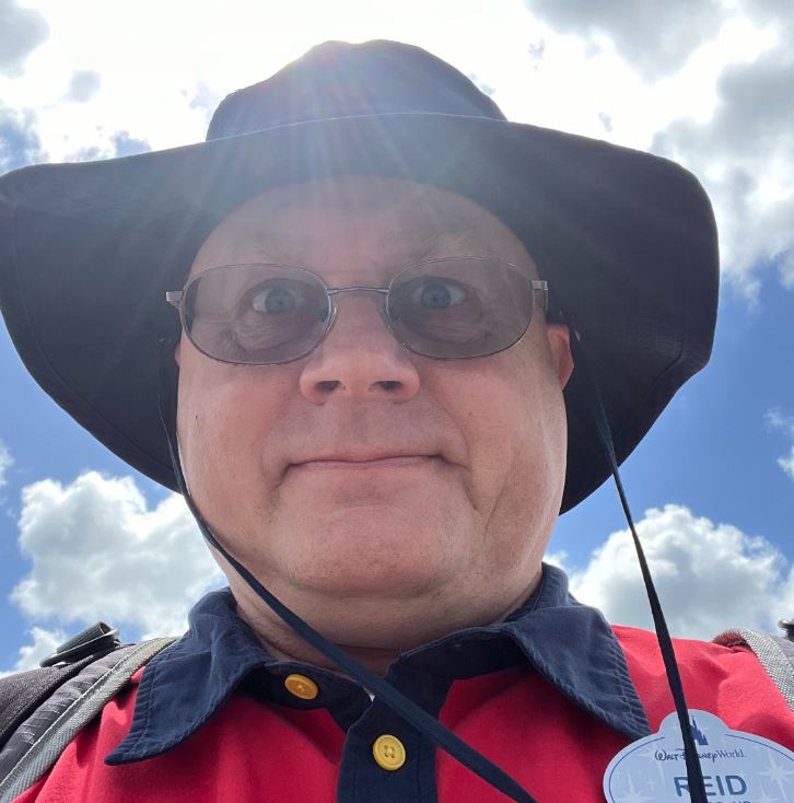middle aged white man with glasses and a black hat wearing a red and navy shirt with a Walt Disney World nametag.