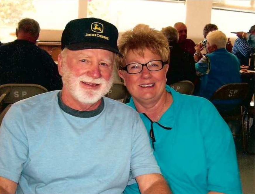 myeloma patient older white man with white beard and mustache wearing John Deere hat and blue tshirt with wife with short hair glasses and turquoise shirt