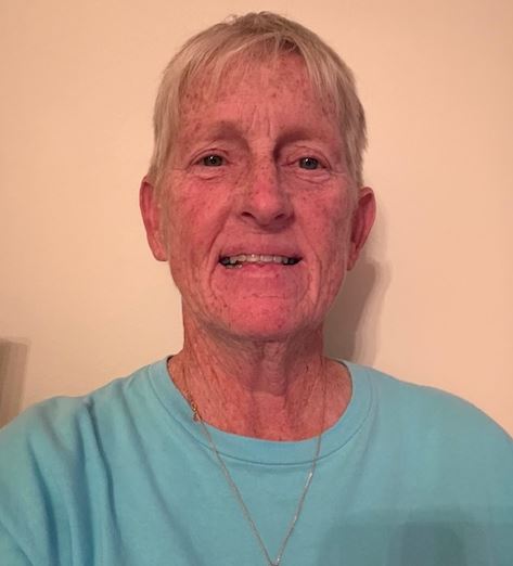 older white woman with short blond hair wearing a necklace and blue tshirt