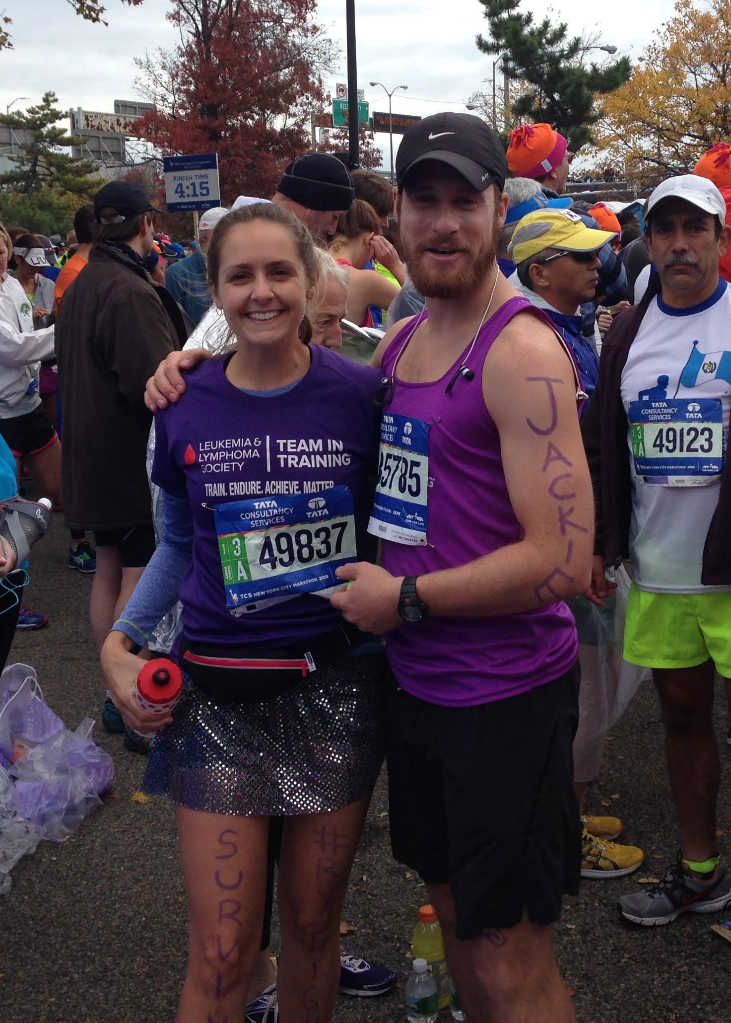 young white woman in a TNT shirt and race number and a sequined skirt with survivor written on her leg standing next to young white man with a black Nike hat beard and mustache
