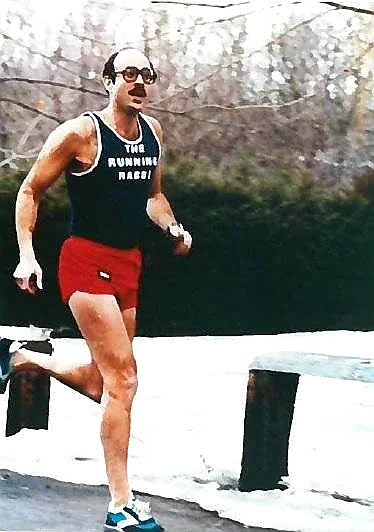 Hirshel middle aged white man balding with black glasses and mustache running in a black tank and red short the running rabbi