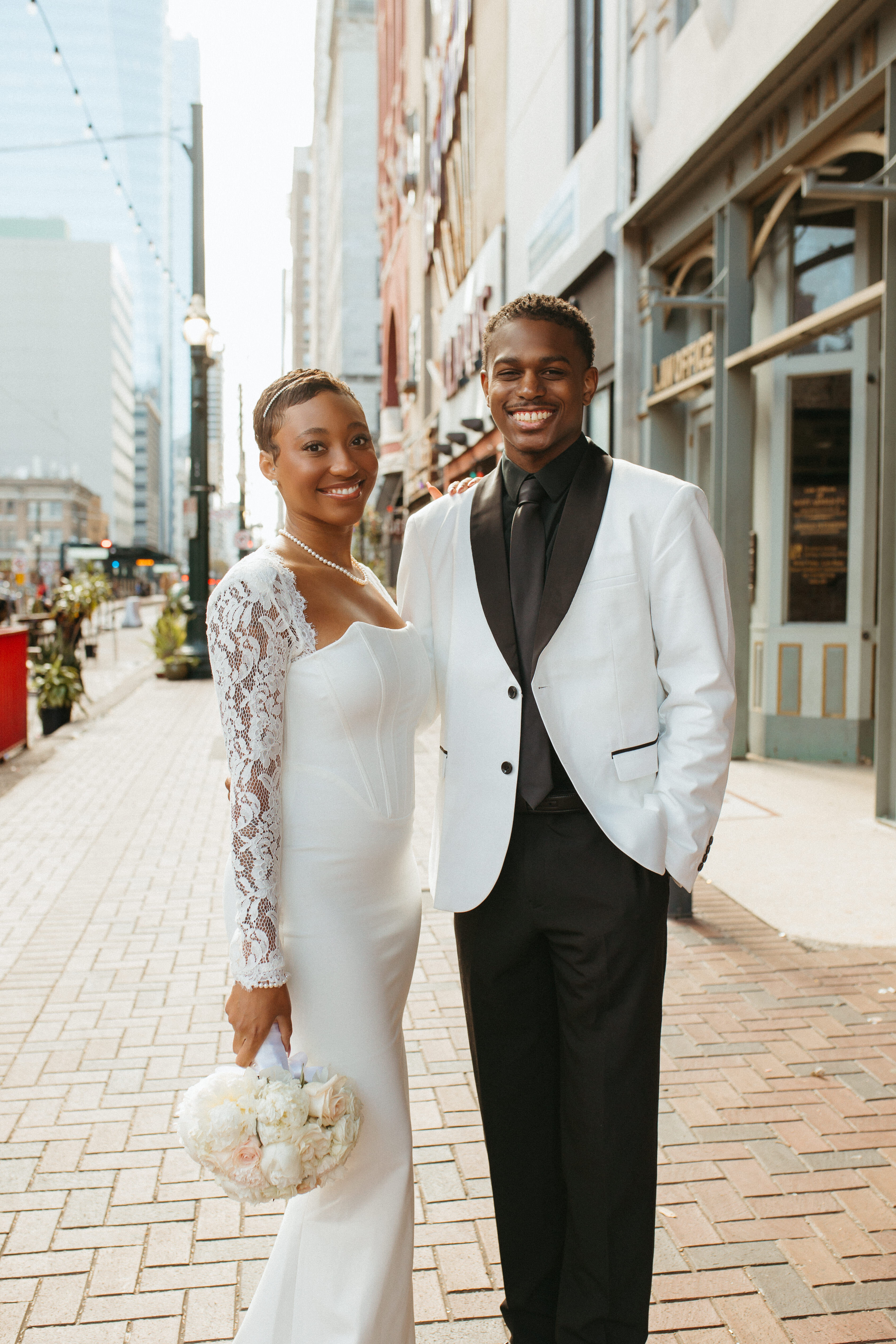 Jayson young black couple in wedding attire white coat black shirt and tie standing outside in a downtown area