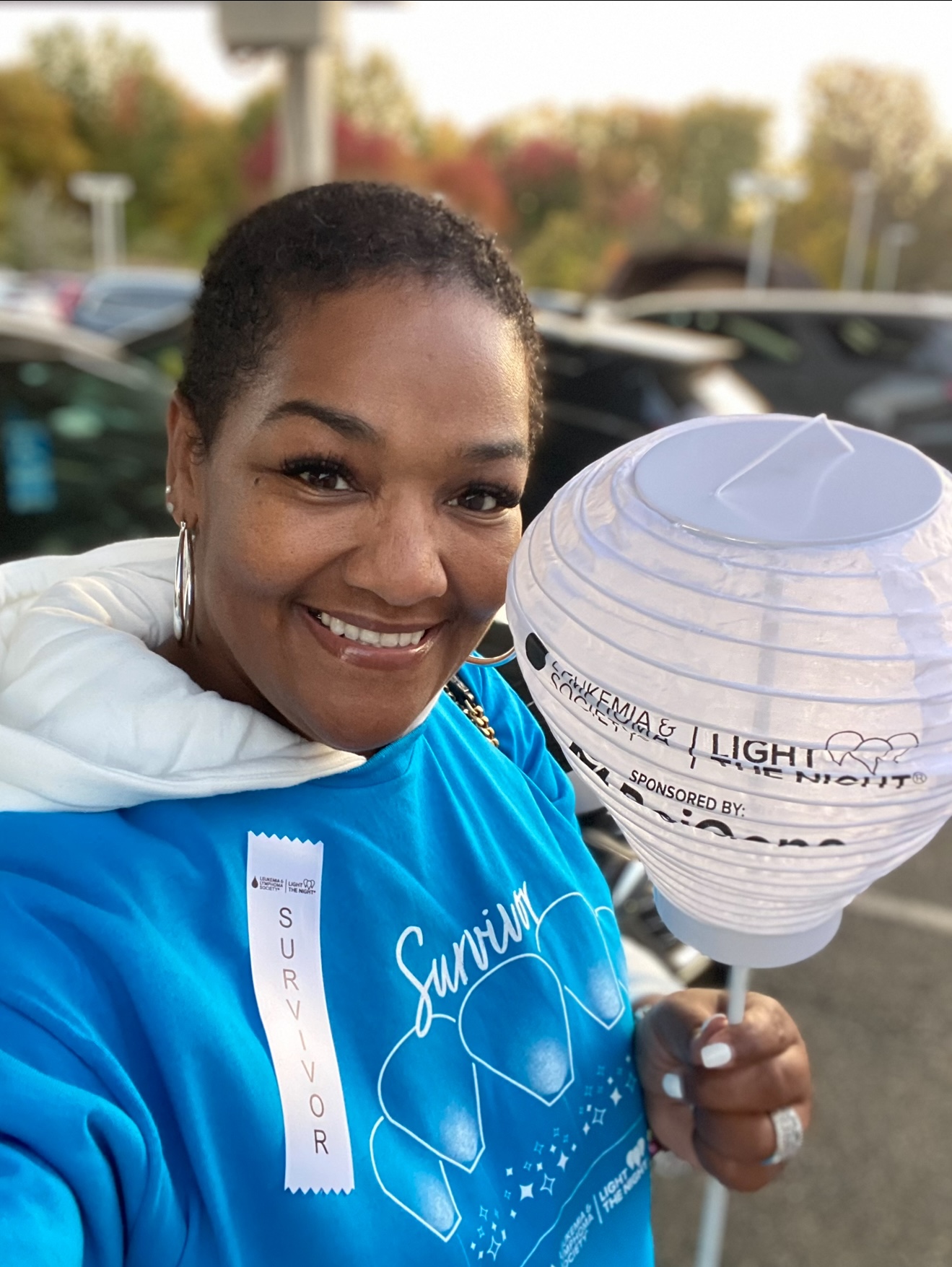 Kenya middle aged black woman with short black hair wearing big hoop earrings and a blue survivor tshirt and white ribbon hold a LTN light