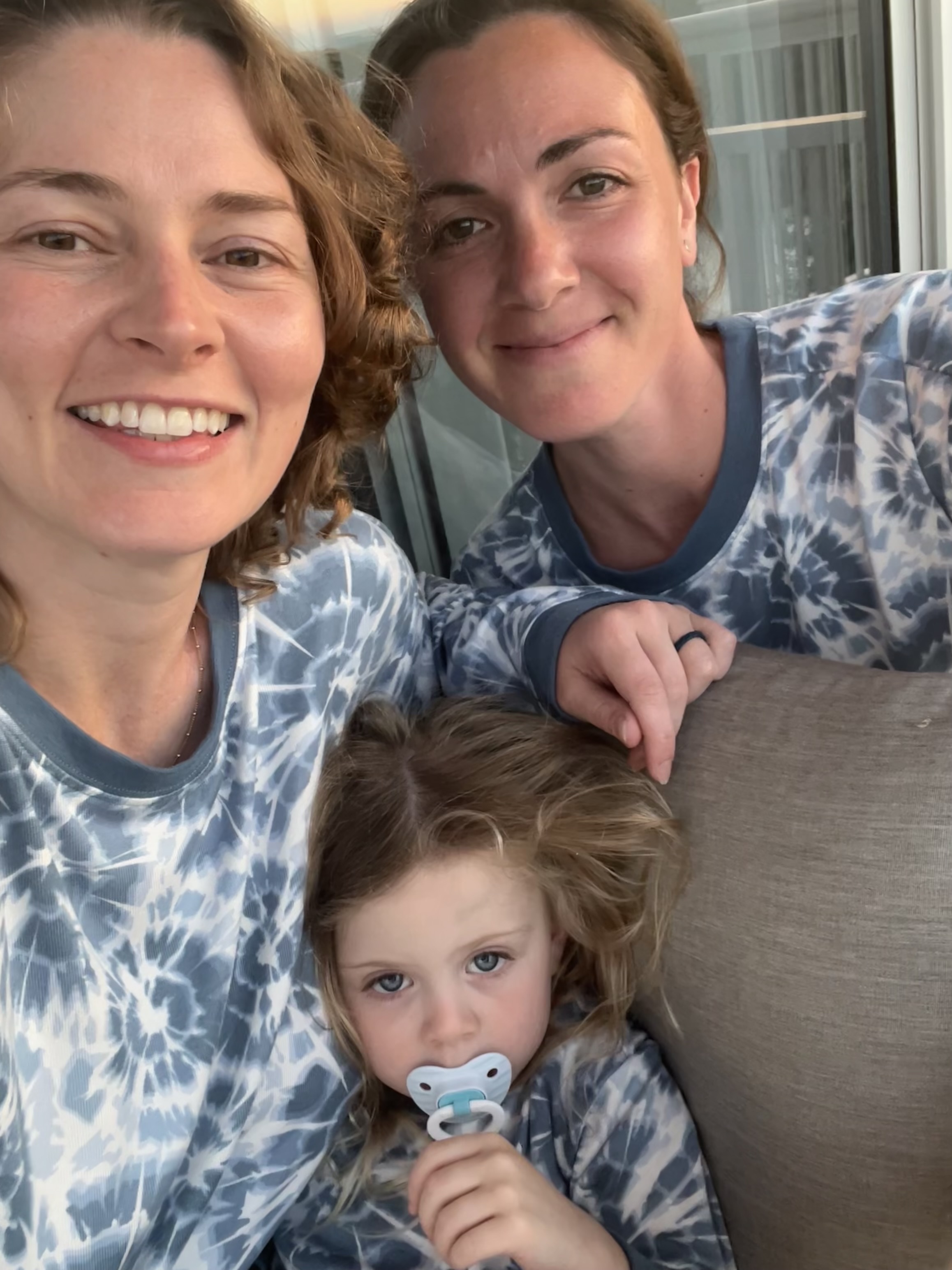 Kimbery two young white women and a little girl all wearing blue tie-dye shirts sitting on a brown sofa