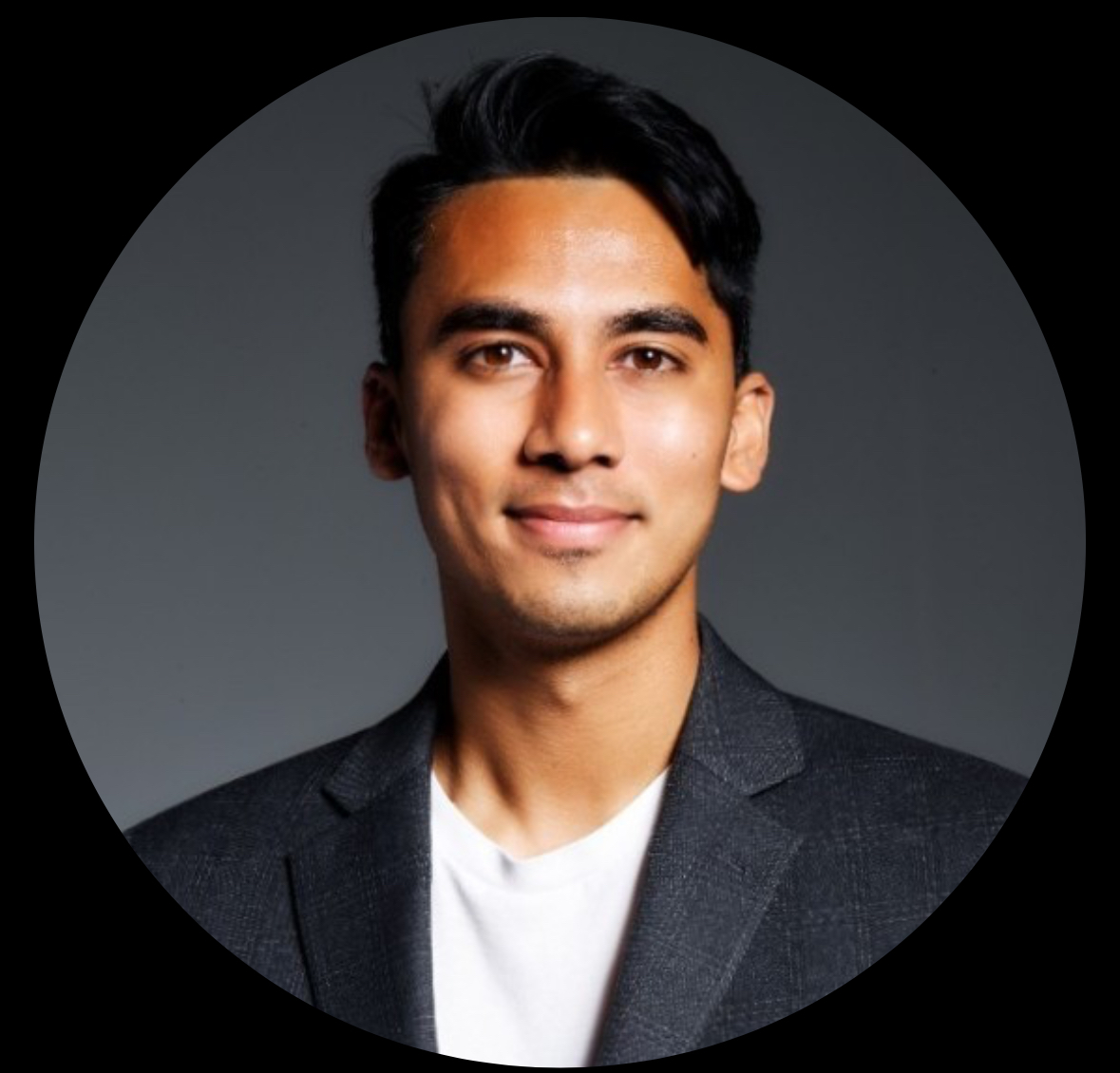 Rohan young man of Indian heritage with dark hair and slight chin stubble wearing a dark gray jacket over a white tshirt.