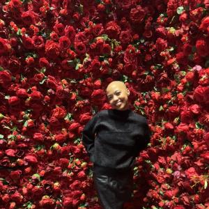 young black woman, bald, dressed in black in front of red roses