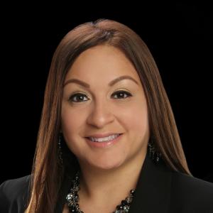 Young hispanic woman with long brown hair in a red top and black jacket wearing a necklace and earrings