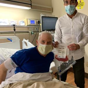 Man in blue shirt and mask in a hospital bed with a medical worker holding a bag of stem cells