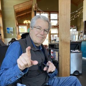 Older white man wearing glasses a denim shirt with a black vest and jeans pointing a finger.jpg