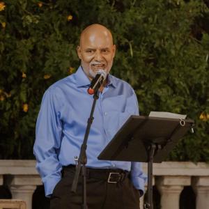 older balding man wearing a blue shirt standing in front of a microphone and podium