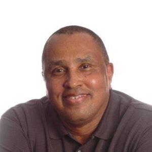 older black man smiling wearing a burgundy colored shirt with his arms crossed