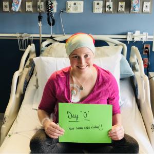 young white woman in a hospital bed wearing a pink shirt, turban and holding a green sign that says new stem cells today