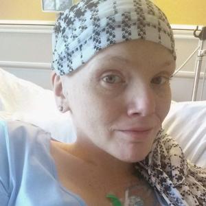 young white woman with a scarf on her bald head wearing a blue shirt laying in a hospital bed