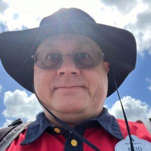 middle aged white man with glasses and a black hat wearing a red and navy shirt with a Walt Disney World nametag.