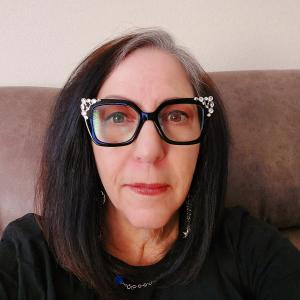 older white woman with dark long hair wearing black chunky glasses with bling on them and a black top