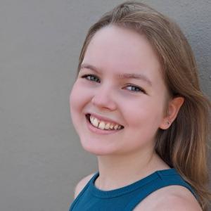 young white girl with brown hair and star earrings with a slight gap in her two front teeth wearing a blue tank top
