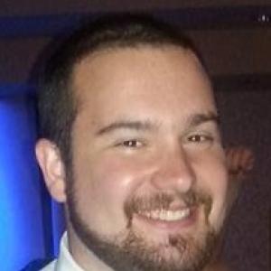 young white man with brown hair beard mustache wearing a white shirt with a blue tie and vest