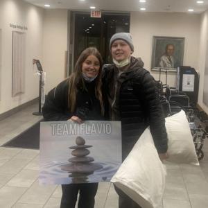 Flavio young hispanic couple she is holding Team Flavio poster and he is holding a pillow both wearing black jackets