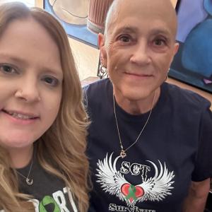 Susanne middle aged white woman with a bald head wearing hoop earrings and a heart necklace and a SCT Survivor t-shirt standing next to a young woman with a nose ring and Support Squad t-shirt