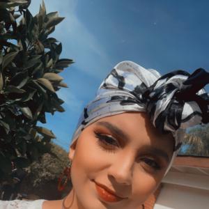 Yesenia young hispanic woman with blue and black headscarf on hoop earrings and a heart necklace wearing a white lacey blouse