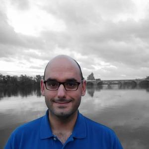 Acute myeloid leukemia survivor wearing a blue buttoned shirt in front of a beautiful landscape