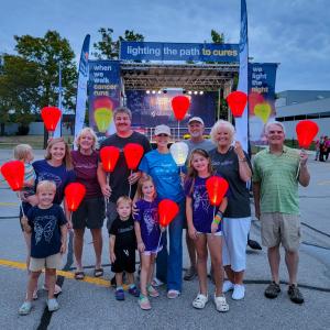 Tricia young white woman wearing a khaki ball cap and blue t-shirt and jeans holding a white LTN balloon surrounded by adutls and children holding orange balloon at a LTN walk