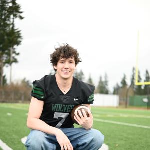 young adult smiling while holding a football on the field wearing a jersey