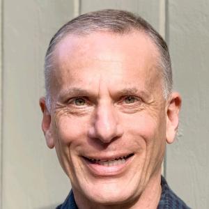 Geoff older white man with graying hair smiling and wearing a blue checked shirt