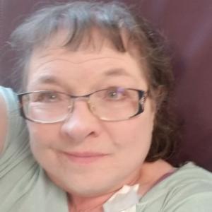 Dixie older white woman with brown hair and glasses wearing a green shirt laying against a brown pillow with an earbud laying on her chest