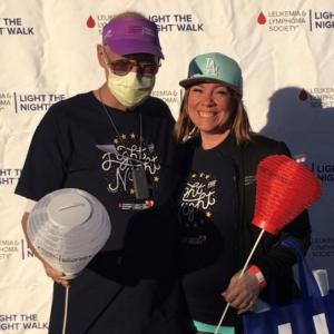 father with AML and daughter standing outside with light the night with hat team in training logos and red and white lanterns
