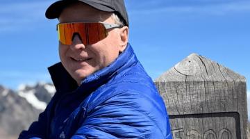 A man with sunglasses stands at a mountain peak at 5,200 meters altitude