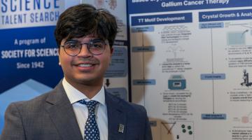 teen researcher stands in front of his project at science competition 