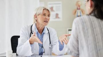 A white doctor sits down and is in the middle of a conversation with a patient