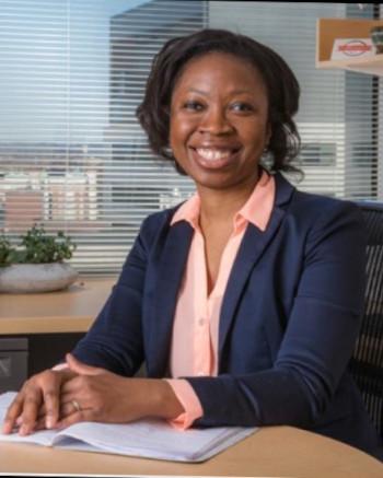 Dr. Oreofe Odejide smiling, sitting, hands folded on desk
