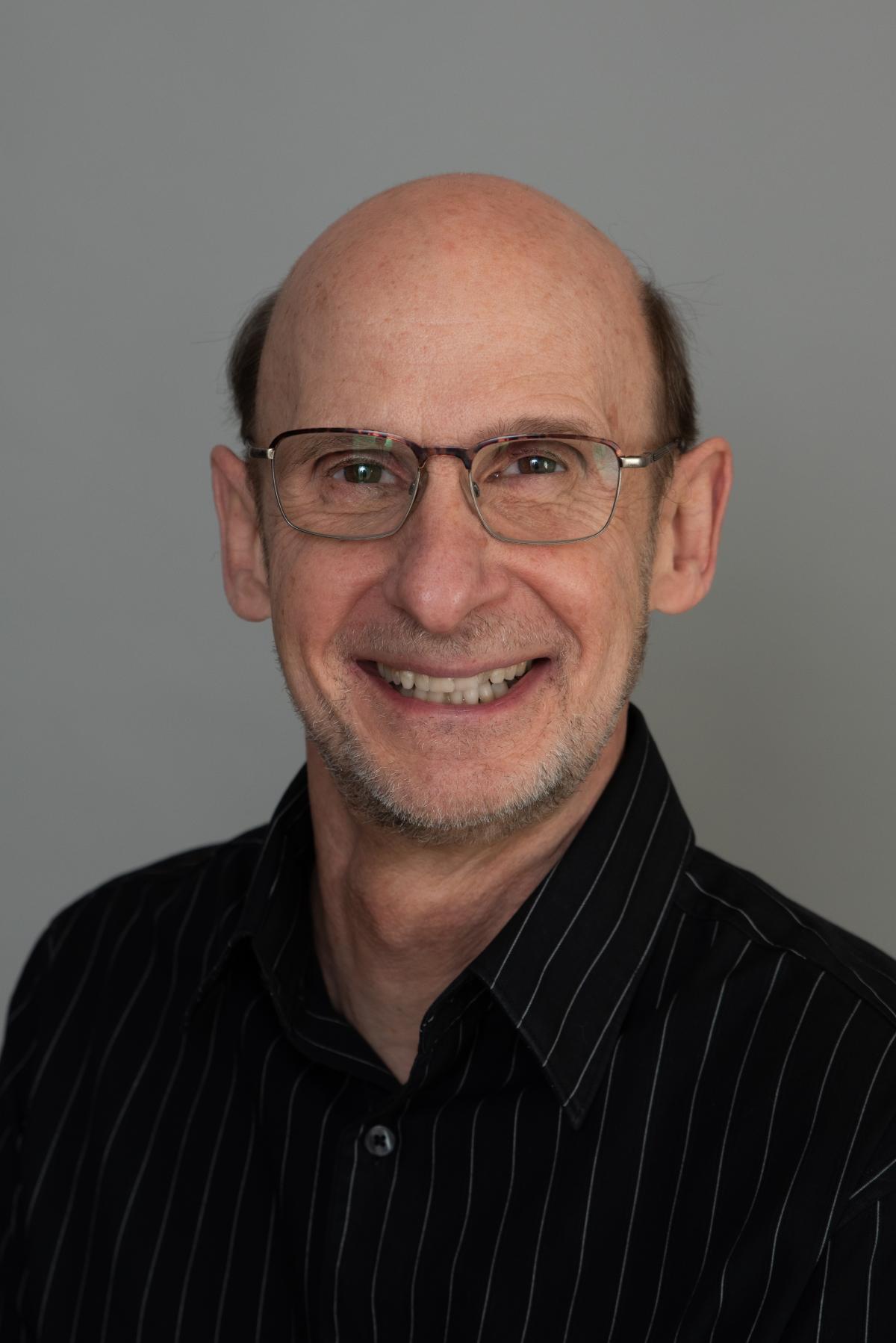A headshot of Steve, a white man with glasses, smiling and wearing a black collared shirt.