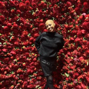 young black woman, bald, dressed in black in front of red roses