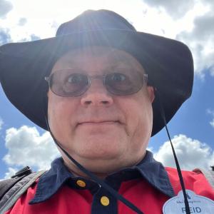 middle aged white man with glasses and a black hat wearing a red and navy shirt with a Walt Disney World nametag.