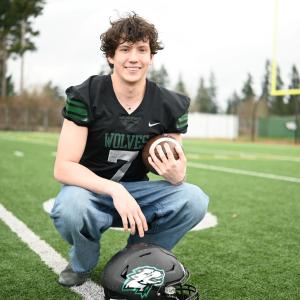 young adult smiling while holding a football on the field wearing a jersey
