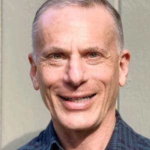 Geoff older white man with graying hair smiling and wearing a blue checked shirt