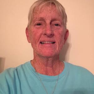 older white woman with short blond hair wearing a necklace and blue tshirt