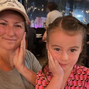 young white woman wearing ball cap and greenish tshirt with daughter in a pink and black top and both have a hand up against their cheeks