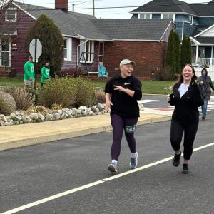 Ally two young white women running along a street one bald and wearing a ball cap both in dark running gear